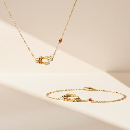 Collier et bracelet assorti en or, orn&eacute;s de fermoirs en forme de fer &agrave; cheval incrust&eacute;s de pierres pr&eacute;cieuses jaunes, oranges et blanches, sur un fond beige doux.